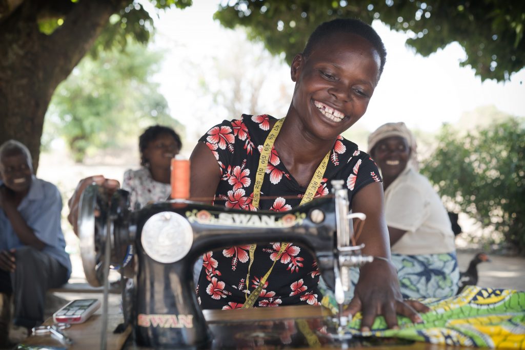 A woman is working on a sewing machine and smiling.
